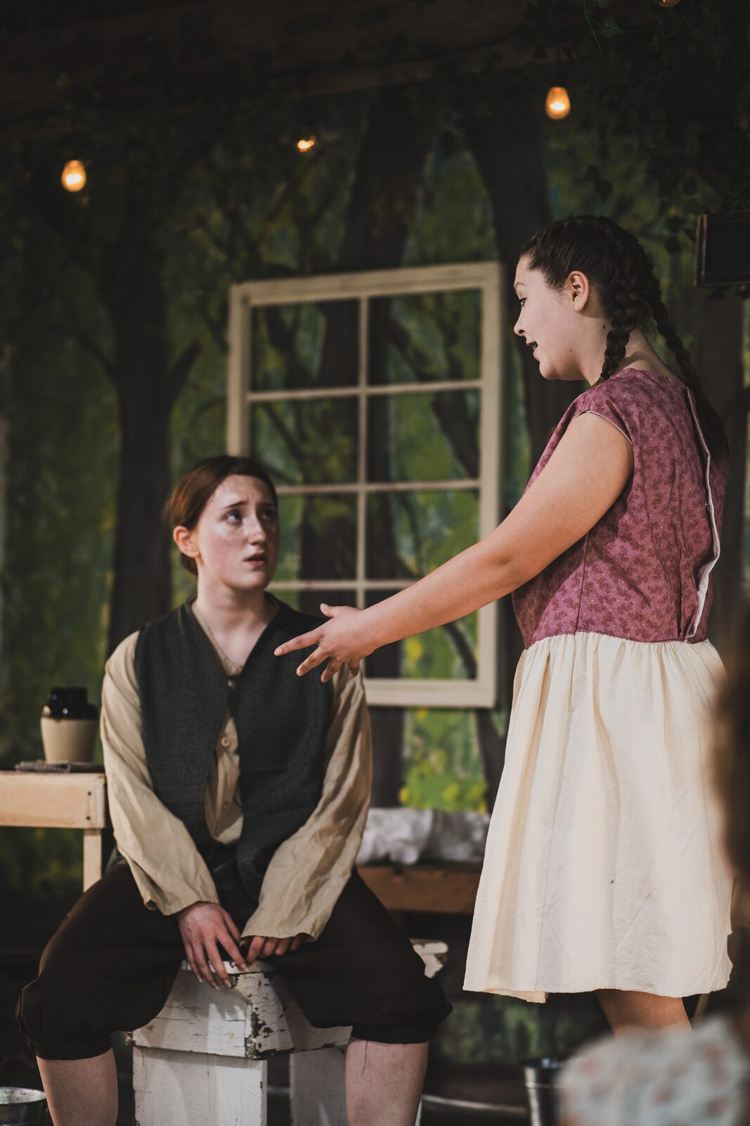 Hansel seated as Gretel speaks to him